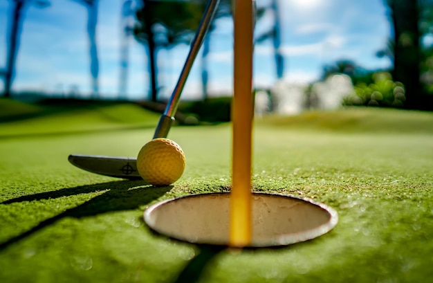 Mini pelota amarilla de golf con un bate cerca del agujero al atardecer