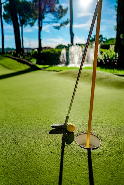 Foto mini pelota amarilla de golf con un bate cerca del agujero al atardecer