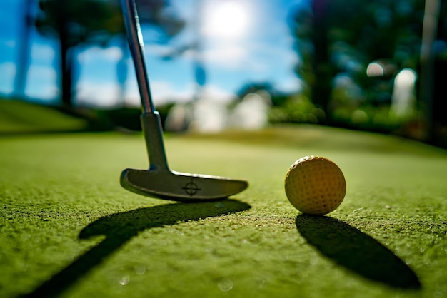 Mini pelota amarilla de golf con un bate cerca del agujero al atardecer