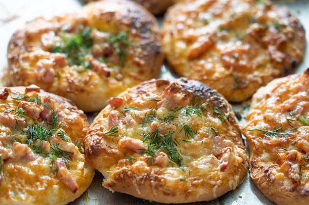 Mini pizzas caseiras assadas recheadas com presunto de queijo e verduras em uma assadeira.