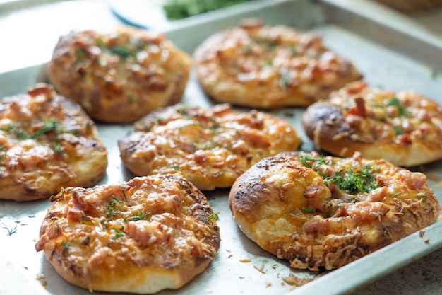 Mini pizzas caseiras assadas recheadas com presunto de queijo e verduras em uma assadeira.