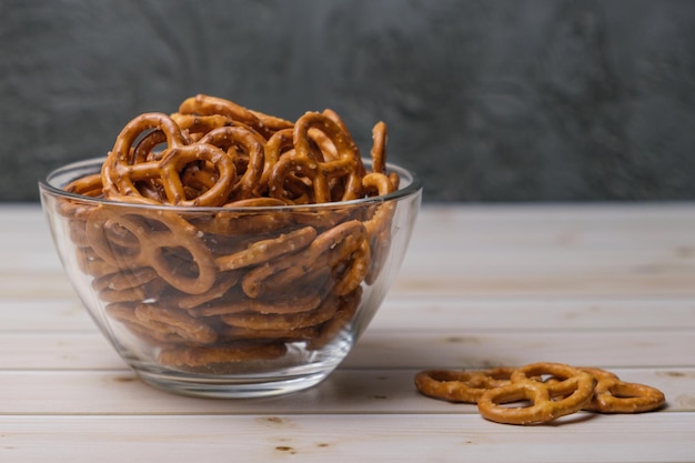 Mini pretzels salados en un recipiente de vidrio profundo sobre una mesa de madera. Merienda popular de cerveza. Espacio para texto.