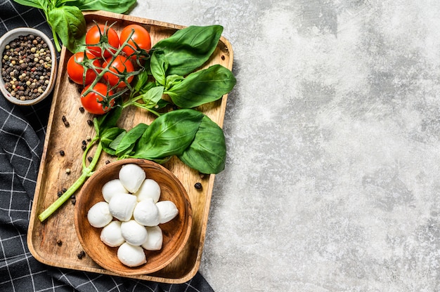 Mini queijo mussarela, folhas de manjericão e tomate cereja, cozinhando a salada caprese. fundo cinza. vista do topo. copie o espaço