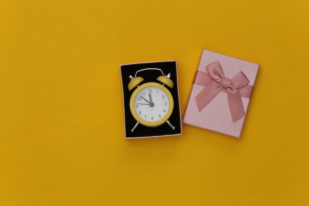 Mini reloj despertador y cajas de regalo sobre fondo amarillo.