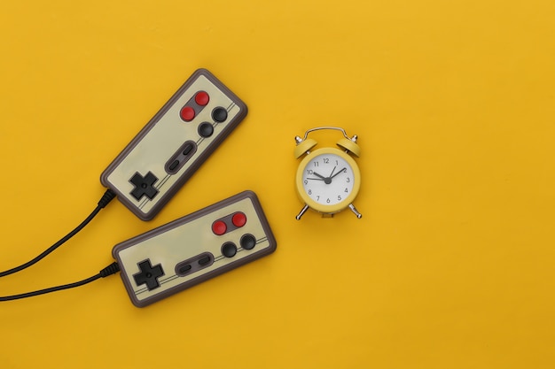 Mini reloj despertador y joysticks retro sobre un fondo amarillo.