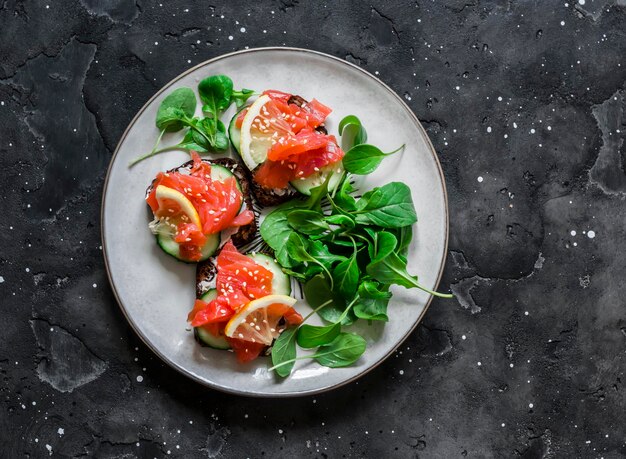 Mini sándwiches con pan de centeno queso crema salmón y pepino sobre un fondo oscuro vista superior Delicioso desayuno tapas aperitivo