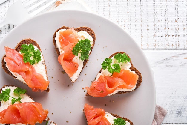 Mini sándwiches con perejil de requesón de salmón y pan de centeno en forma de corazones Comida creativa casera del día de San Valentín Amor diseño de desayuno Enfoque selectivo y espacio de copia