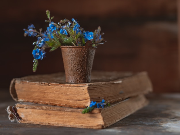 Mini-strauß wilder blumen in einem dekorativen eimer auf alten büchern am dorffenster.