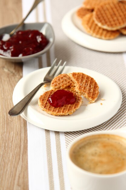 Mini stroopwafels (jarabes) en un plato con una taza de café y mermelada