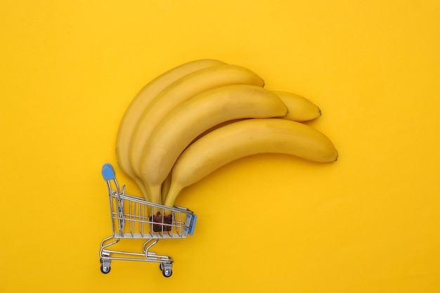 Mini-Supermarktwagen mit reifen Bananen auf gelbem Hintergrund.