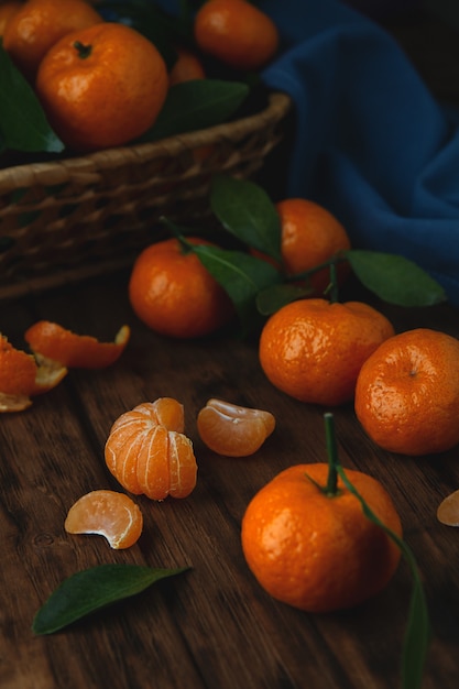 Mini tangerinas com folhas em uma cesta e em uma mesa de madeira.