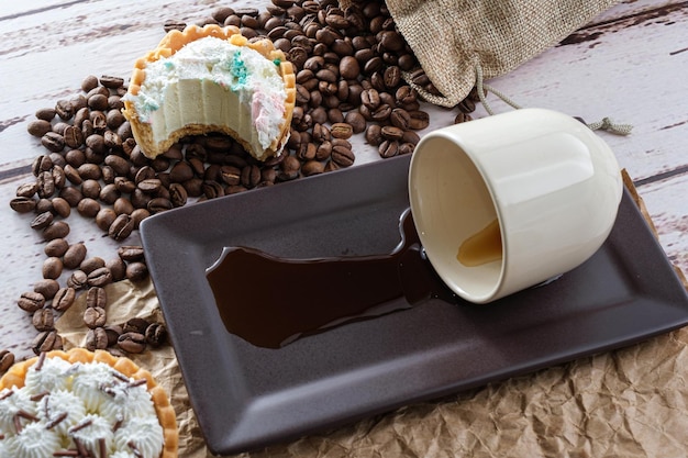 Mini tarta de hojaldre mantecoso y ganache de chocolate blanco con un bocado, junto a una taza de café volcada (vista superior).