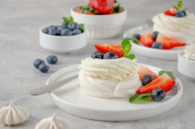 Mini tarta de merengue Pavlova con crema batida y bayas frescas encima en un plato sobre un fondo de hormigón gris. Postre de verano. Copie el espacio.