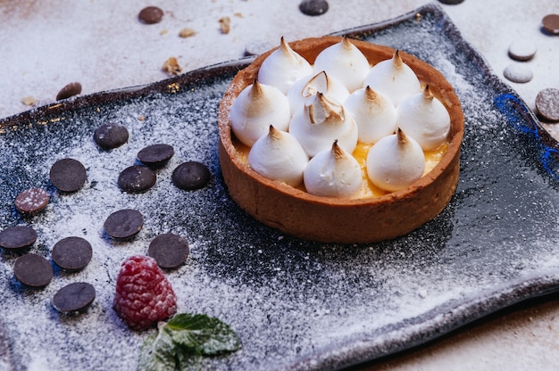 Mini tartaleta con mermelada de frutas y merengue Tarta con merengue italiano y crema sobre plato negro Hermoso desayuno casero del desierto