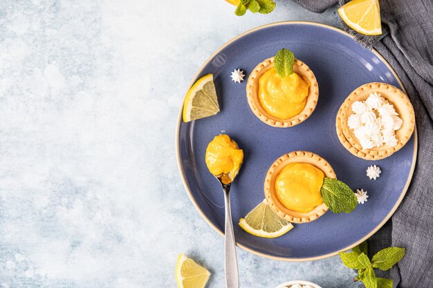 Mini tartas de cuajada de limón decoradas con menta y rodajas de limón en placa de cerámica azul