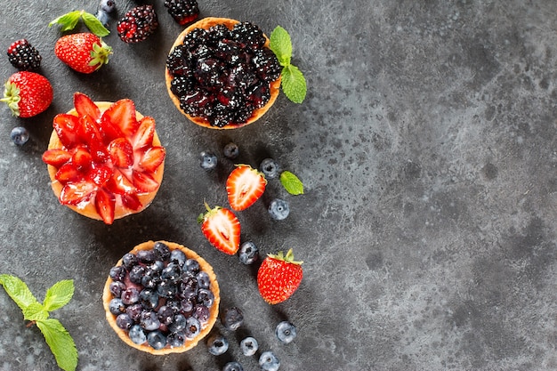 Mini tartas recién horneadas con frutos rojos sobre una mesa. Hornear frutas de verano. Copie el espacio. Vista superior.
