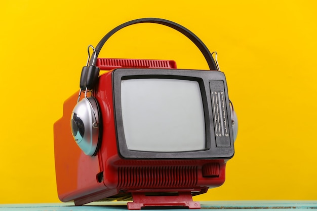 Mini televisor portátil antiguo retro rojo con auriculares sobre fondo amarillo.