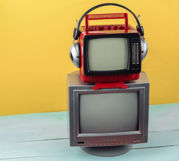 Mini televisores portátiles antiguos retro con auriculares sobre fondo azul amarillo.