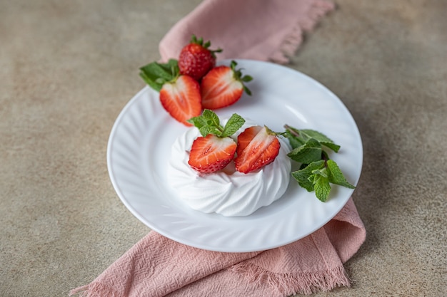 Mini tortas de merengue Pavlova con fresas y menta en una placa, superficie de hormigón
