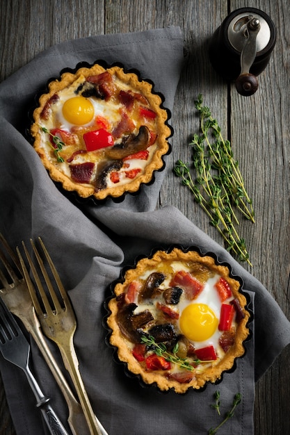 Mini-Torte mit gebackenem Schinken, Pfeffer, Pilzen und Wachteleiern in cremiger Sauce auf einem Holzständer