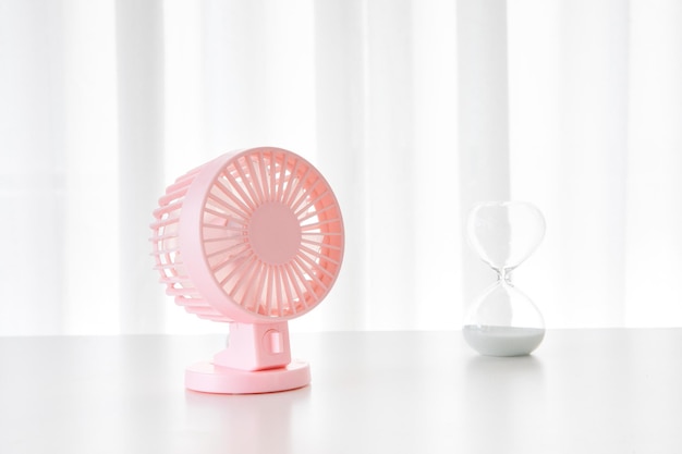 Foto mini ventilador de metal rosa y un reloj de arena sobre una mesa blanca