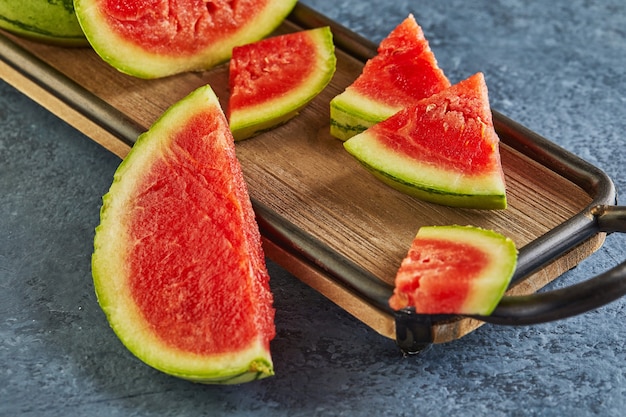 Mini-wassermelone mit geschnittenen keilen auf einem holzständer auf einem blau.