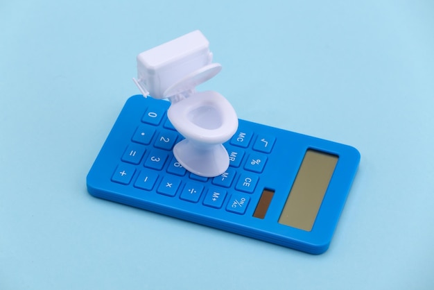 Mini weiße Toilette und Taschenrechner auf blauem Hintergrund. Minimalismus.