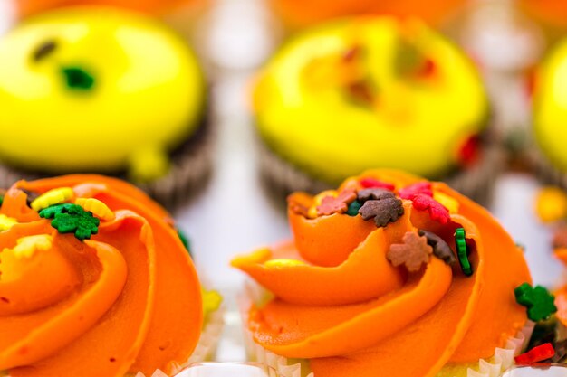 Miniatur-Capcakes mit gelbem und orangefarbenem Zuckerguss und Streuseln.