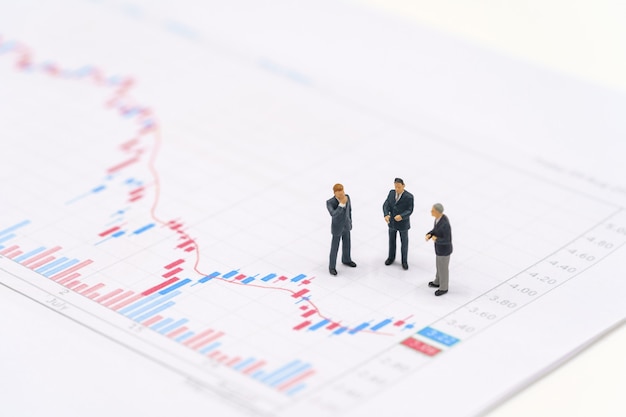 Miniatur-Geschäftsleute, die auf dem Börsendiagramm stehen, sind die Hintergrundinvestitionsinvestitionsinvestition. Verwendung als Hintergrundgeschäftskonzept mit Kopierraum und Leerraum.