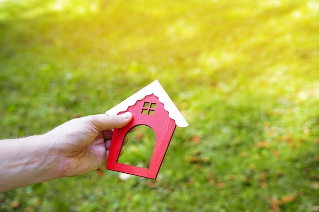 Miniatur-Holzhaus in den Händen eines Mannes im Freien Immobilienkonzept Umweltfreundliches Zuhause Kauf eines Gehäuses außerhalb der Stadt Rotes Dach Selektiver Fokus