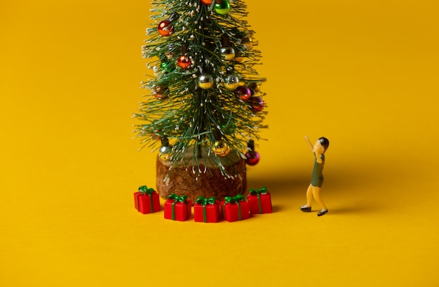 Miniatur-Jungenfigur steht in der Nähe von y roten Weihnachtskugeln auf gelbem Hintergrund