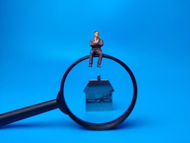 Miniatur Peoplehouse Schlüsselanhänger und Lupe auf blauem Hintergrund Immobilienkonzept