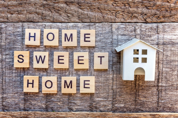 Foto miniatur-spielzeug-modellhaus mit der aufschrift home sweet home buchstaben wort auf holzuntergrund