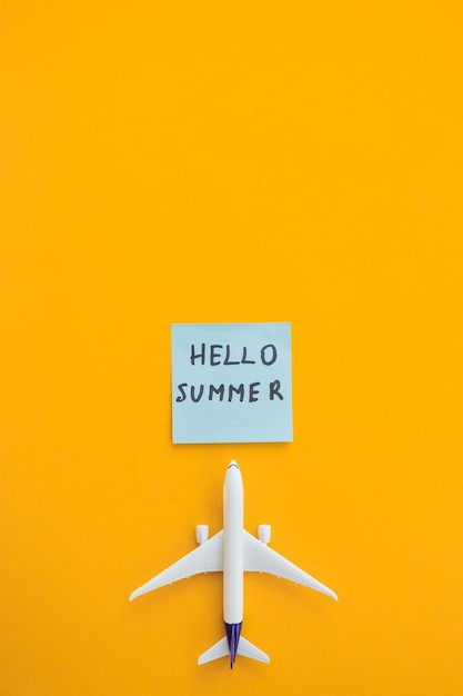 Miniatur-Spielzeugflugzeug auf farbigem Hintergrund und Wort Hallo Sommer Reise mit dem Flugzeug