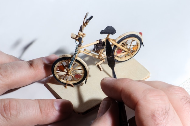 Miniatura da bicicleta de madeira no fundo branco. processo de artesanato, mão de artesão segurando a ferramenta.