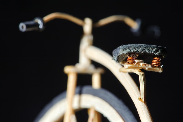 Miniatura de bicicleta de madeira centavo-farthing em fundo preto. Macro artesanato detalhe tiro do assento da bicicleta. Bicicleta da velha escola com roda grande.