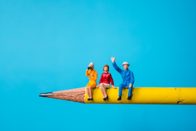 Miniatura de homem e mulher sentada no lápis amarelo usando como negócio e conceito social