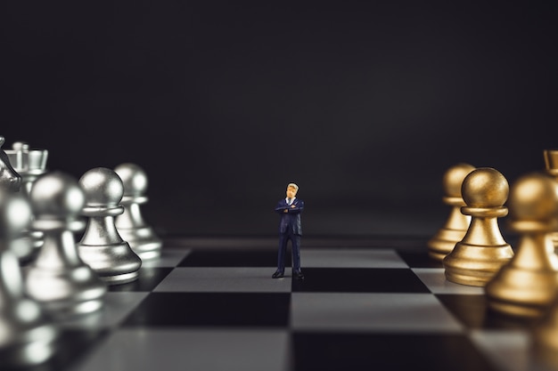 Foto miniatura de líder no meio do conceito de equipe ou pessoal. chefe que está na frente da xadrez do ouro no tabuleiro de xadrez com luminosidade reduzida.