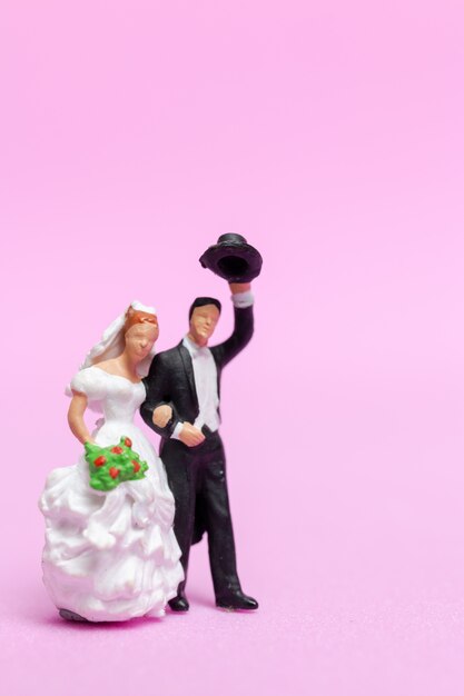 Miniatura personas boda, novios pareja sobre fondo rosa,