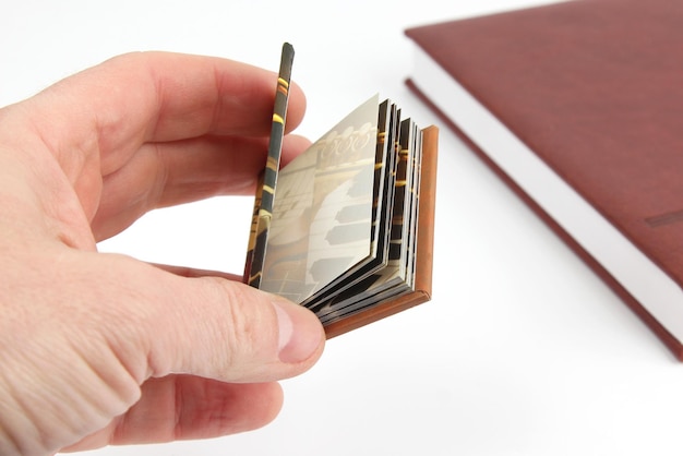 Miniaturbuch in der Hand auf dem Hintergrund der üblichen Bücher