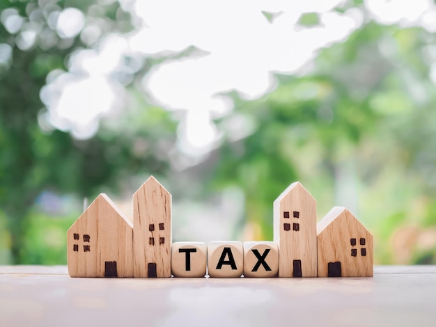 Miniaturhaus und Holzklötze mit dem Wort TAX Das Konzept der Steuerzahlung für Haus und Eigentum
