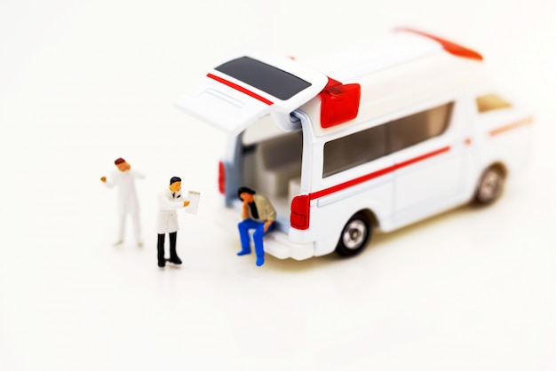 Miniaturleute: Doktor und Patient, die mit Krankenwagen stehen.