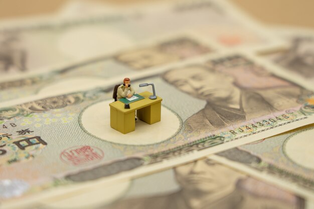 Miniaturleute-Geschäftsmänner, die mit japanischen Banknoten im Wert von 10.000 Yen sitzen