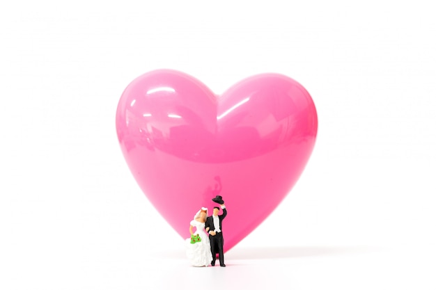 Miniaturleute verbinden mit rosa Herzen auf weißem Hintergrund