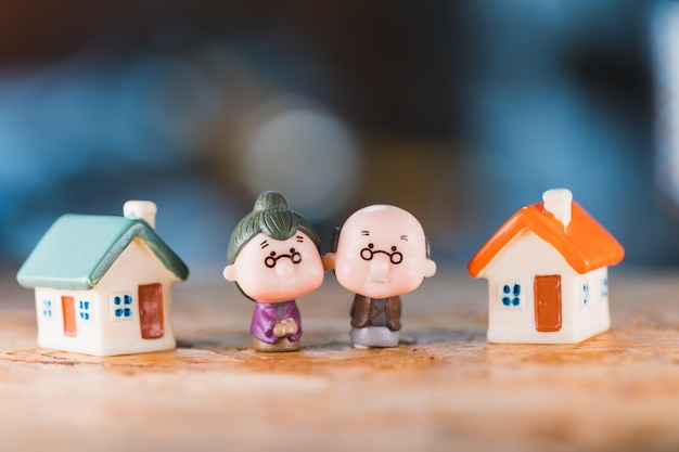 Miniaturmenschen, älterer Mann und Frau, die mit Mini-Haus stehen, das als Arbeitsrenten- und Versicherungskonzept verwendet