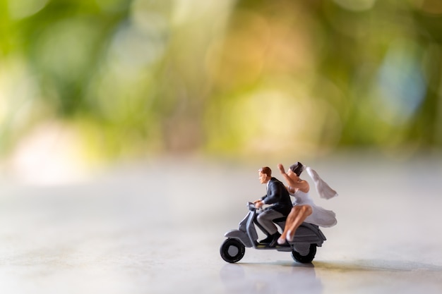 Miniaturmenschen: Braut und Bräutigam im Freien mit grünem Bokeh-Hintergrund und Kopierraum für Text