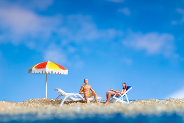 Miniaturmenschen, die sich am Strand sonnen, Sommerzeitkonzept