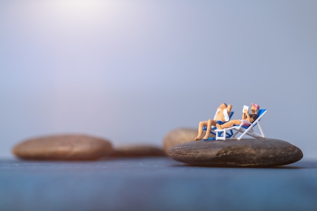 Miniaturmenschen, die sich am Strand sonnen, Sommerzeitkonzept