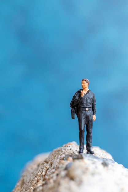 Miniaturmenschen-Geschäftsmann, der auf dem Felsen mit blauem Hintergrund steht