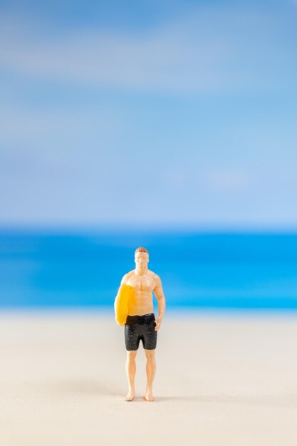 Miniaturmenschen in Badeanzug und mit einem gelben Surfbrett am Strand